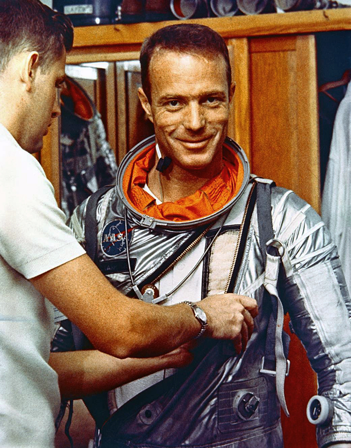 Dressed in his silver pressure suit, Carpenter smiles for the camera as a technician checks the suit over