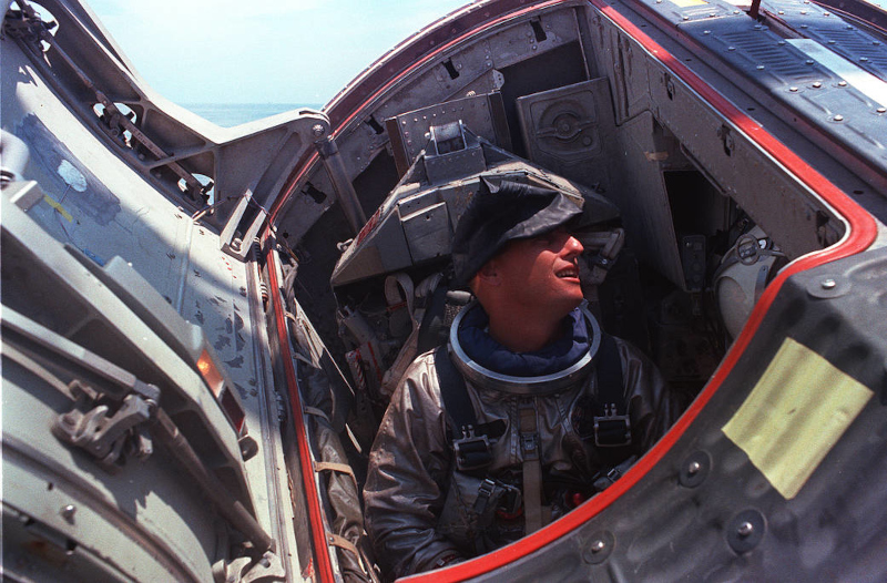 Pete Conrad peers out of the open hatch of a training version of the Gemini capsule that is about to be lowered into the ocean for water egress training