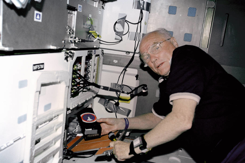 Glenn looks towards the camera as he works on an experiment aboard STS-95