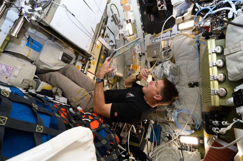 Jeremy Hansen floats in Artemis II, with food in one hand and a tablet screen in the other