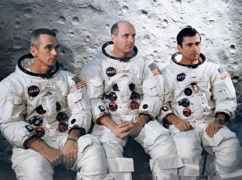 Group portrait of the Apollo 10 crew seated in their space suits during training at KSC, with a lunar backdrop